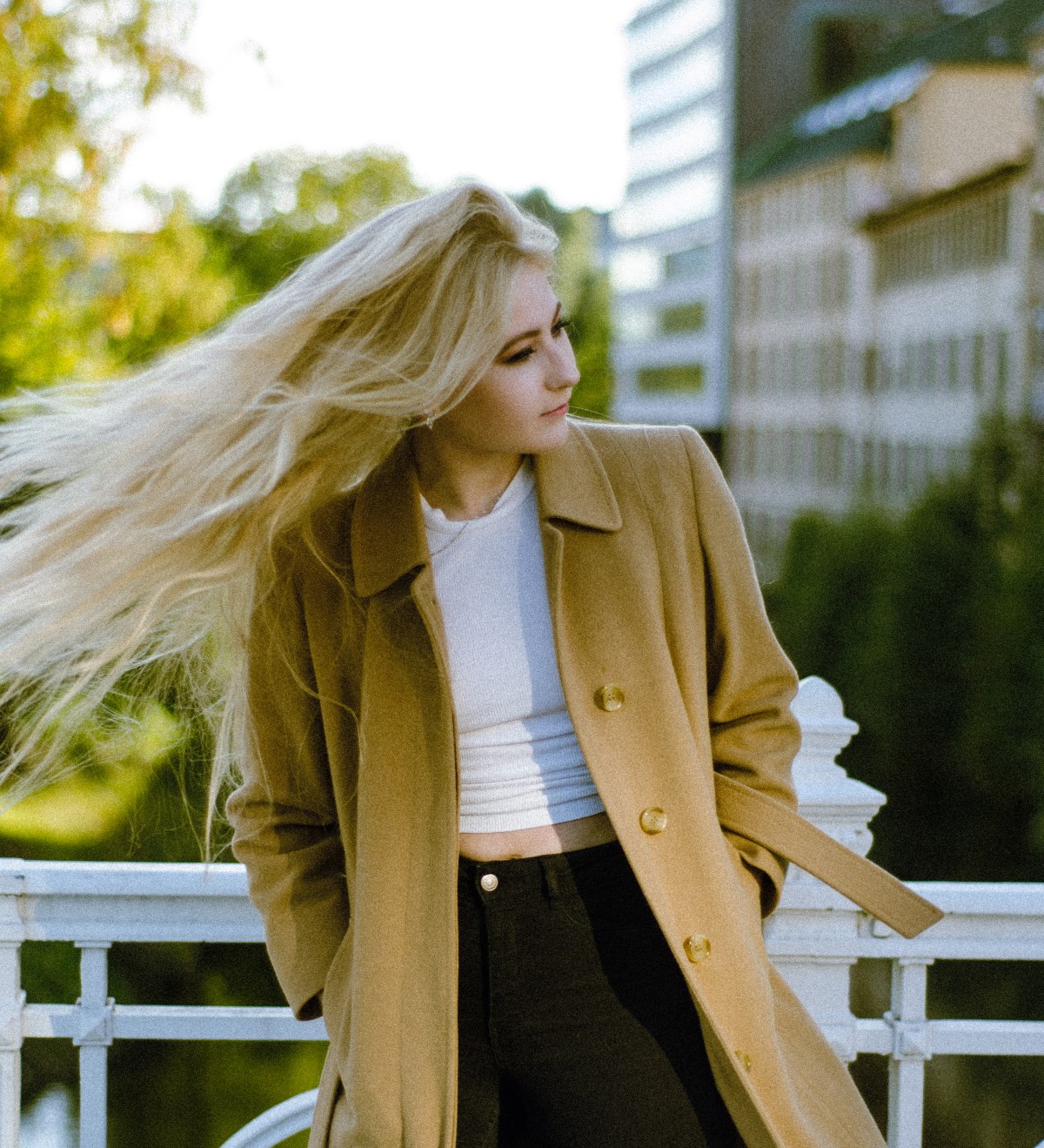 Photoshoot with a lady swirling her blond hair, weaing a trench coat and black jeans.
